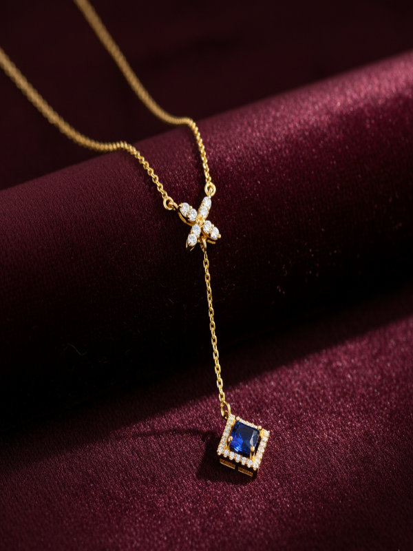Gold necklace with a blue gemstone pendant on a purple fabric background